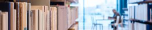 library books on a shelf with person sitting at a desk in the background