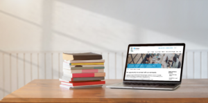 Laptop open to the BCcampus Grants and Calls for Proposals page beside stack of books on wooden table
