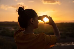Person looking at a sunset and doing a heart hand sign