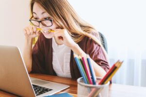 Person biting pencil in front of laptop