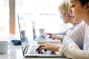 2 people side by side at laptops in brightly lit room