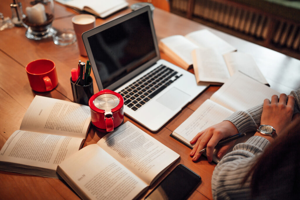 Person with arms folded working at wooden desk with laptop and red coffee cups