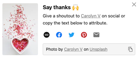 screen capture of pop up window in Unsplash that reads "Say thanks - give a shoutout to Carolyn V on social or copy the text below to attribute". Various social media icons are followed by a link to the photographer's work. The photo being given attribution is on the left. It is of a white ceramic heart shaped bowl filled with pink, red and white sprinkle candies.