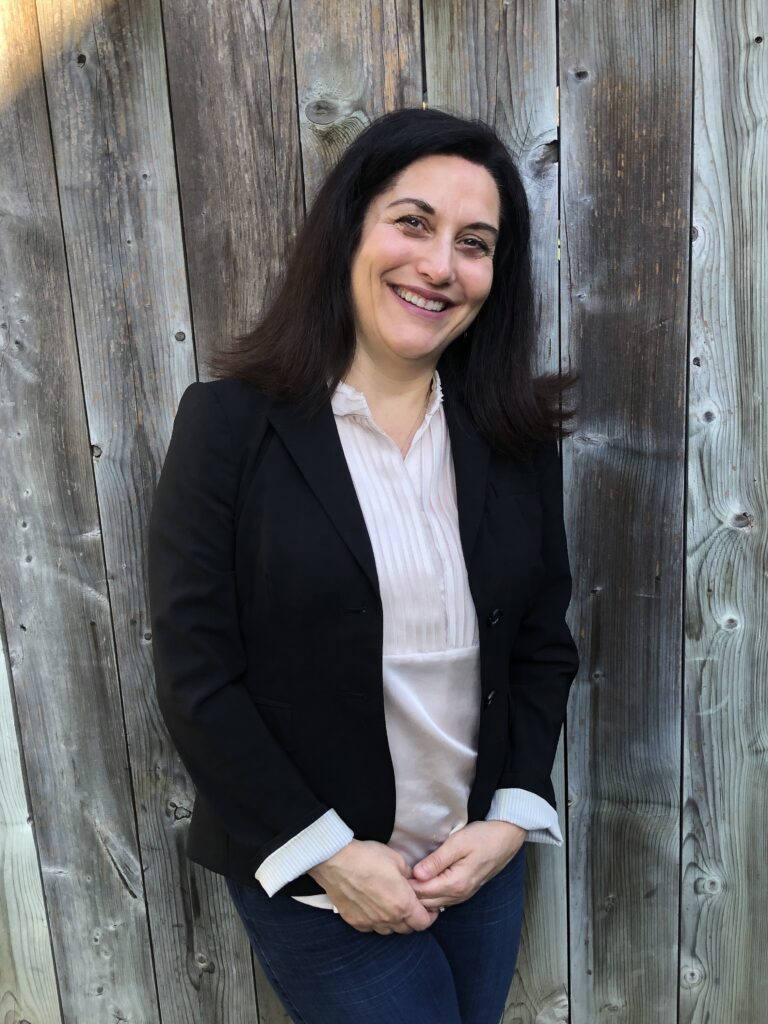 Monica smiling in front of a wooden fence.