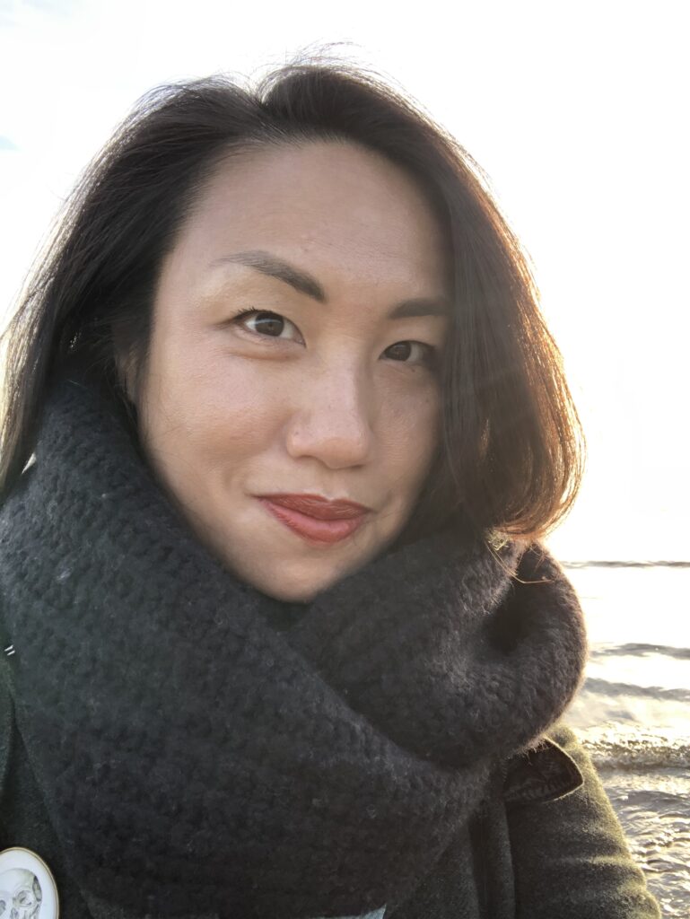 Elle, wrapped in a thick black scarf, smiles on beach