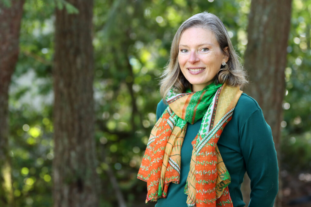 Heather Burke smiles and stands with a forest of trees behind her. 