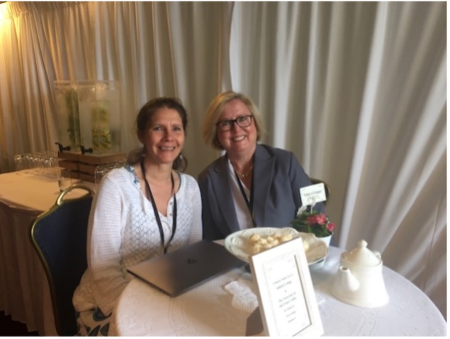 Maureen and Theresa sit side by side at a round table that holds tea and white truffles.