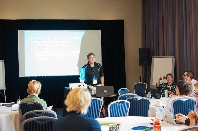 Rod Lidstone; stands in front of projector screen surrounded by people at conference tables while Jennifer Kirkey sits, raising a mug and smiling to the camera. Beside Jennifer is Arthur "Gill" Green.