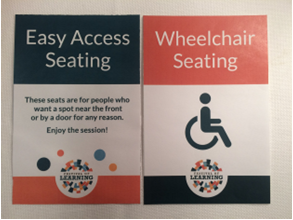 2 signs are shown.

First one reads "Easy Access Seating: These seats are for people who want a spot near the front or by a door for any reason. Enjoy the session!" 

Second one reads: "Wheelchair Seating" with symbol.